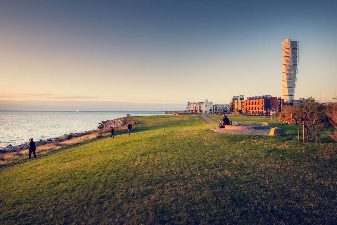 People walking and hanging out at Ribersborg beach during sunset. Västra Hamnen and Turning Torso are visible in the background. Photo: Werner Nystrand